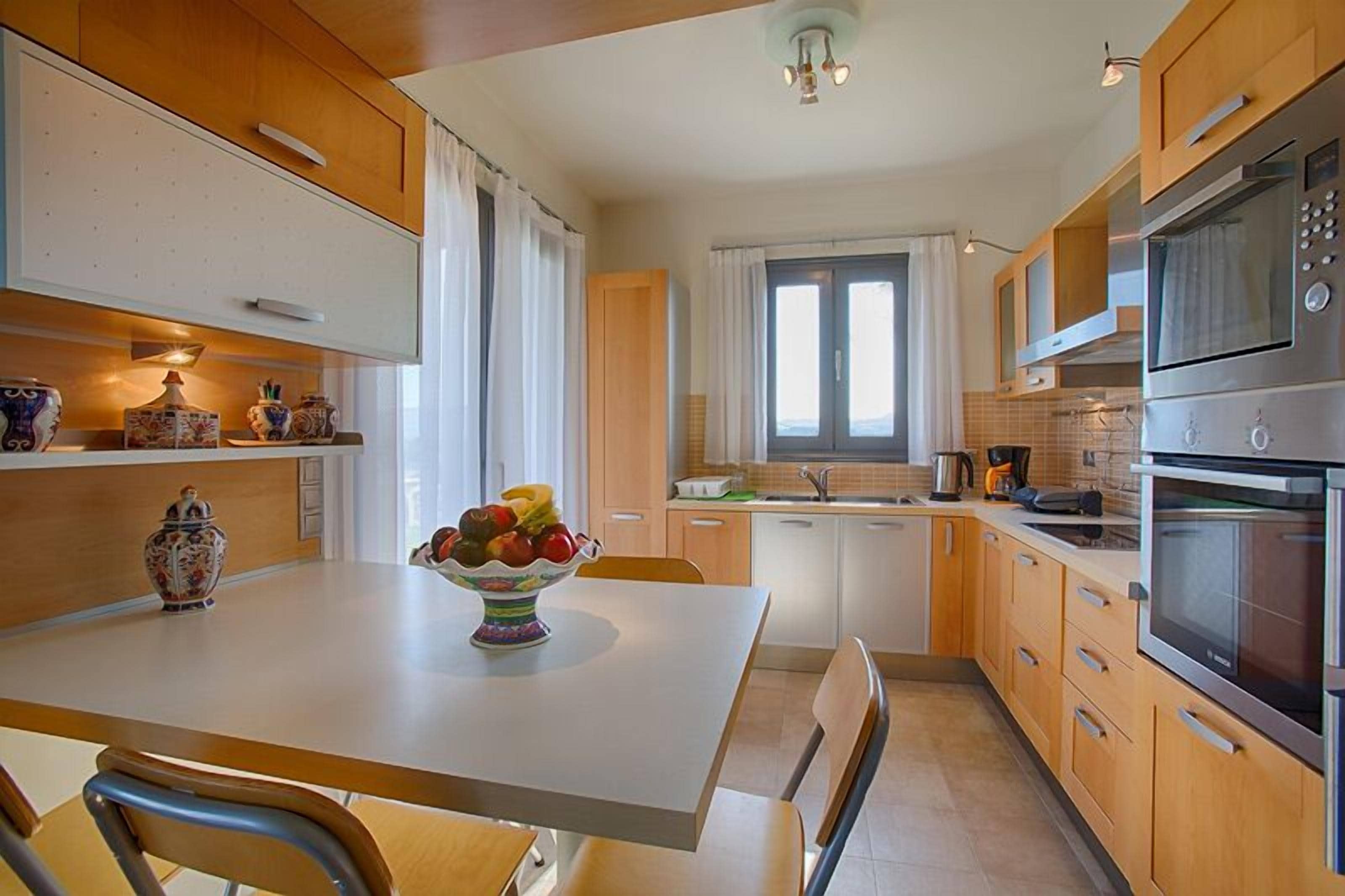 A modern kitchen with wooden cabinets, a white countertop, and a bowl of fruit.