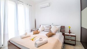 A hotel room with a bed, bedside tables, a nightstand, and an air conditioning unit on the wall. - Haraki Villas (Rhodes)