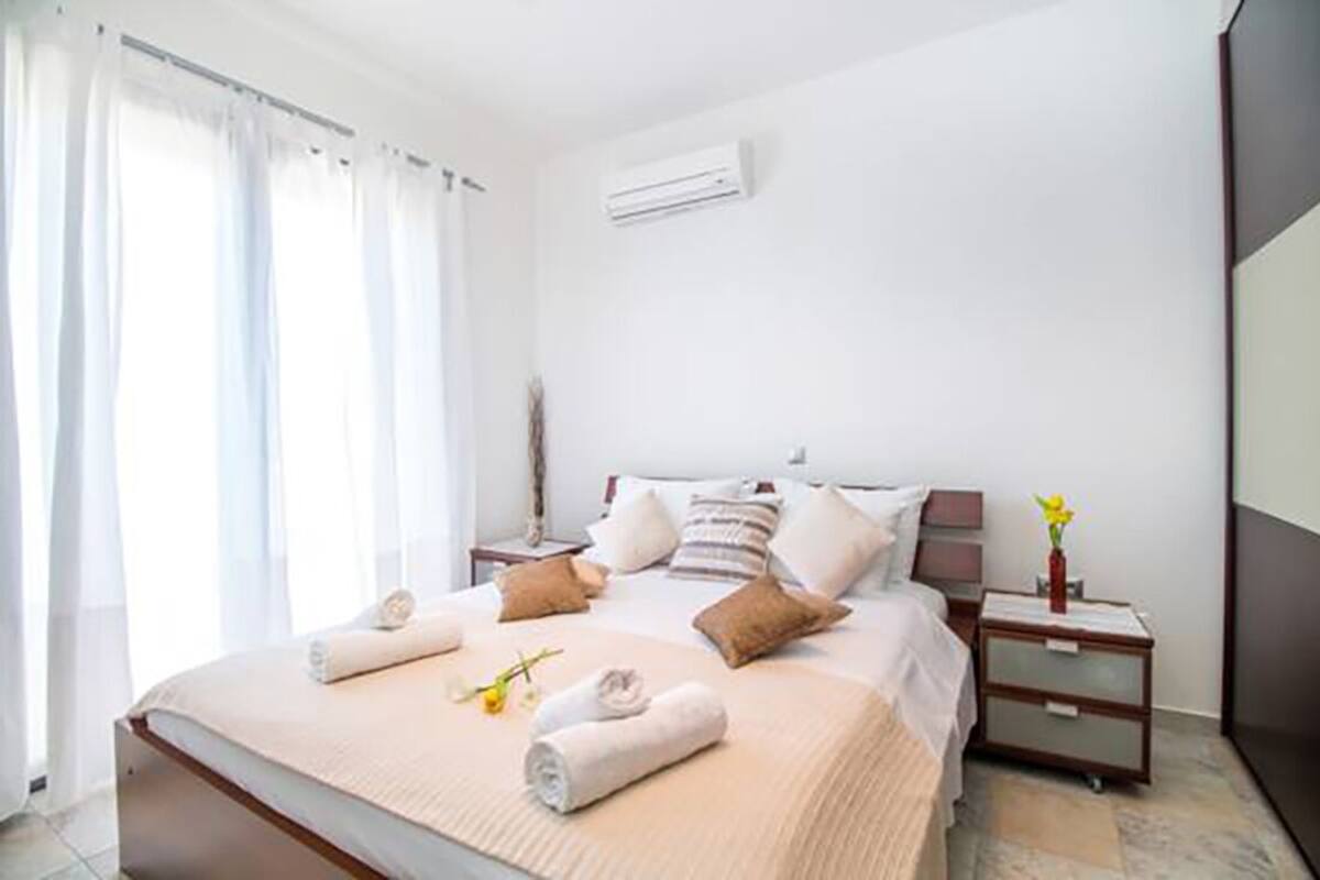 A hotel room with a bed, bedside tables, a nightstand, and an air conditioning unit on the wall.