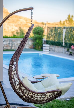 A wicker hanging chair with white cushions by a poolside. - Haraki Villas (Rhodes)