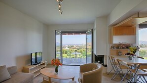 A modern living room with a TV, sofa, and coffee table. There's a balcony with a view of the countryside. - Haraki Villas (Rhodes)