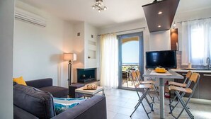 A modern living room with a sofa, a TV, a dining table with chairs, and a fireplace. - Haraki Villas (Rhodes)