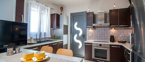 A modern kitchen with dark cabinetry, a stainless steel refrigerator, a built-in oven, and a flat-screen TV.