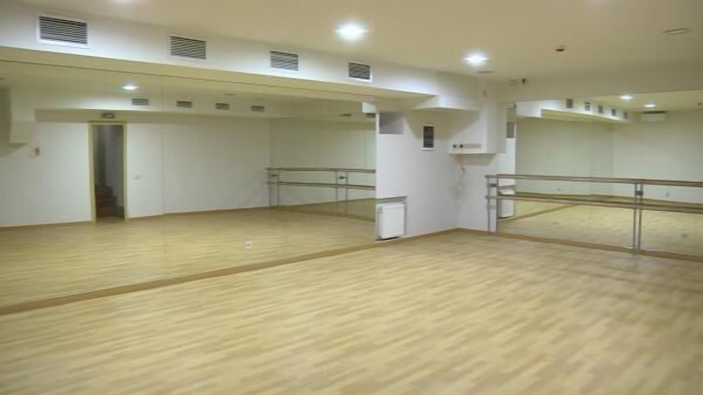 A spacious dance studio with wooden floors, mirrored walls, and ceiling vents.