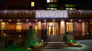 A hotel entrance with a staircase leading up to the doors, surrounded by a well-lit garden area and a string of lights above. - Zagrava Hotel (Dnipro)