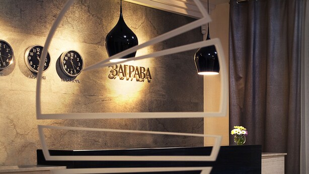 A modern reception area with a stone wall, a black reception desk, and three wall clocks. - Zagrava Hotel (Dnipro)