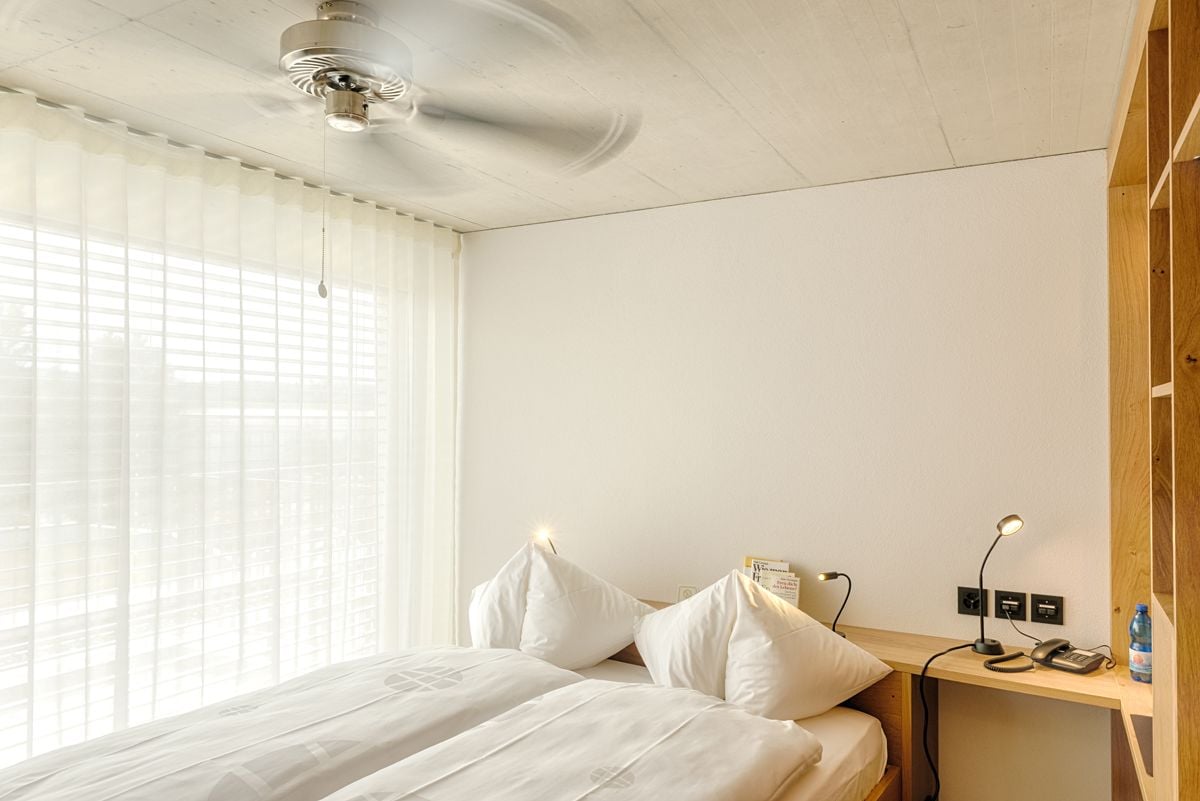 A hotel room with a bed, a desk with a lamp, a telephone, and a ceiling fan.