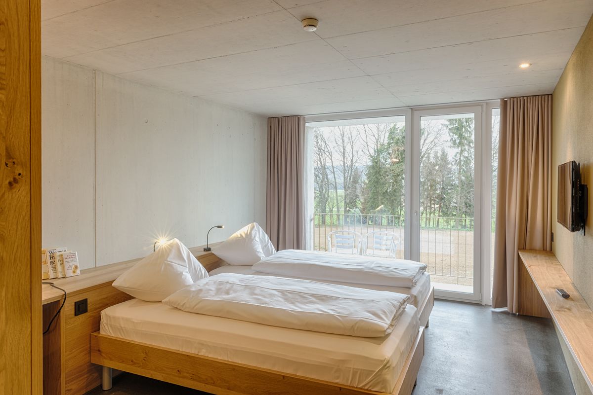 Habitación de hotel con dos camas, televisión y balcón con vistas a árboles.
