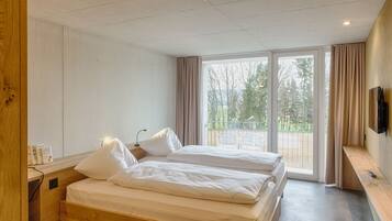 Ett hotellrum med två sängar, en TV och en balkong med utsikt över träd.