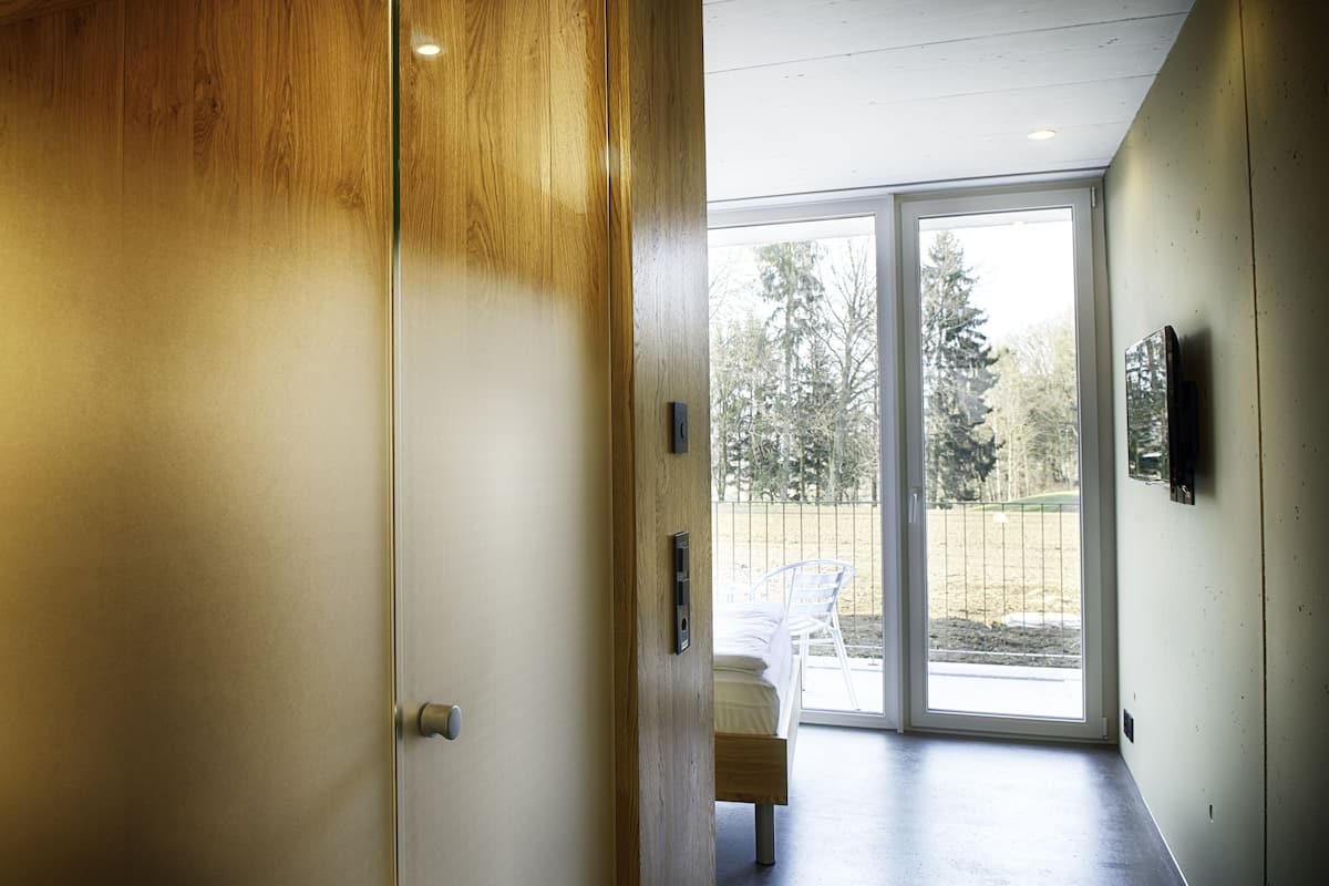 Un intérieur moderne avec une porte en bois, une porte-fenêtre coulissante donnant sur un espace extérieur et un téléviseur fixé au mur.