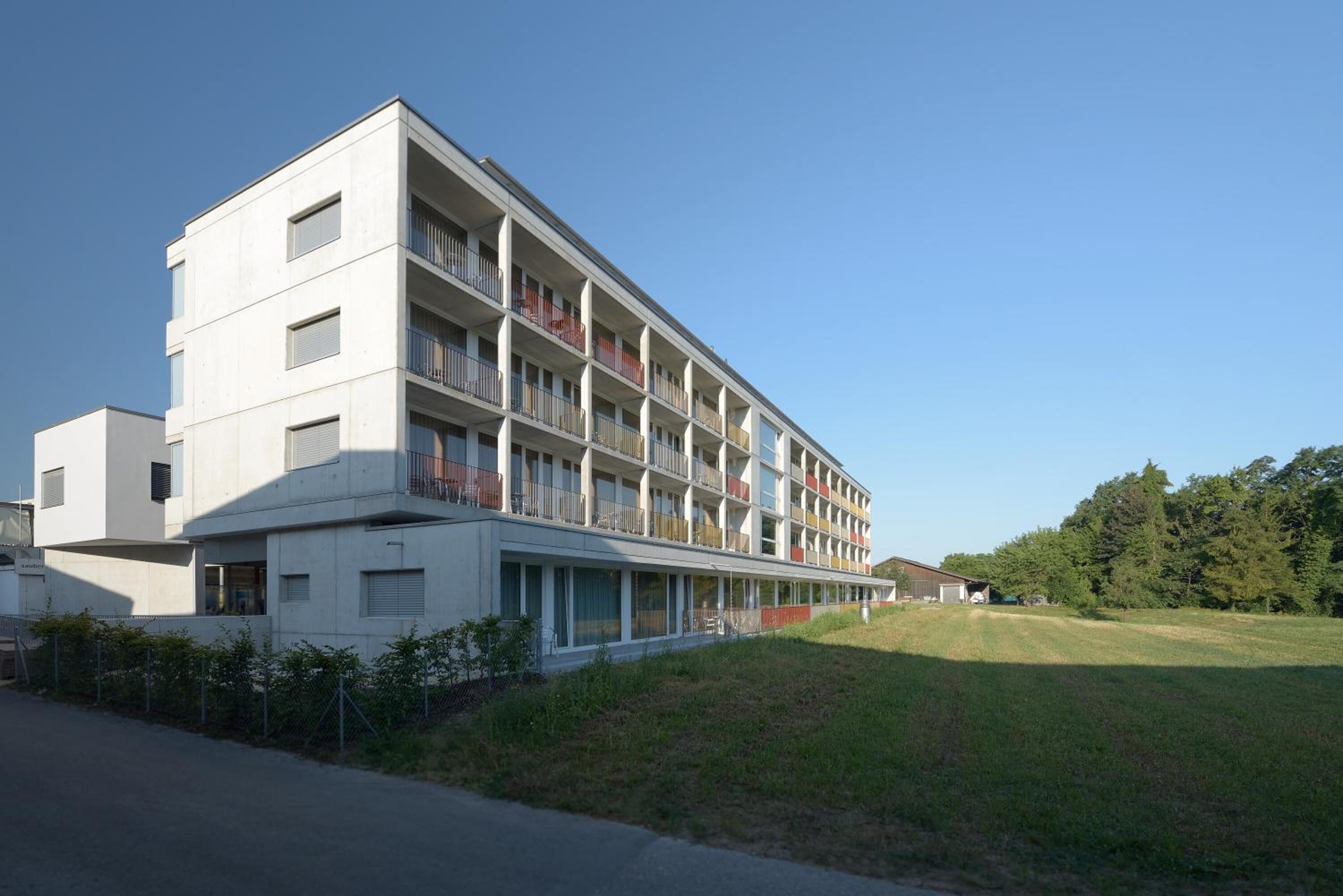 A multi-story hotel with balconies, a flat roof, and a grassy area in front.
