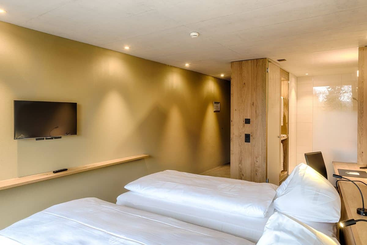 Une chambre d’hôtel avec un lit, un téléviseur fixé au mur et un panneau en bois sur le mur.