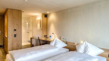 A hotel room with two beds, a wooden desk, a shower area, and a small bathroom.