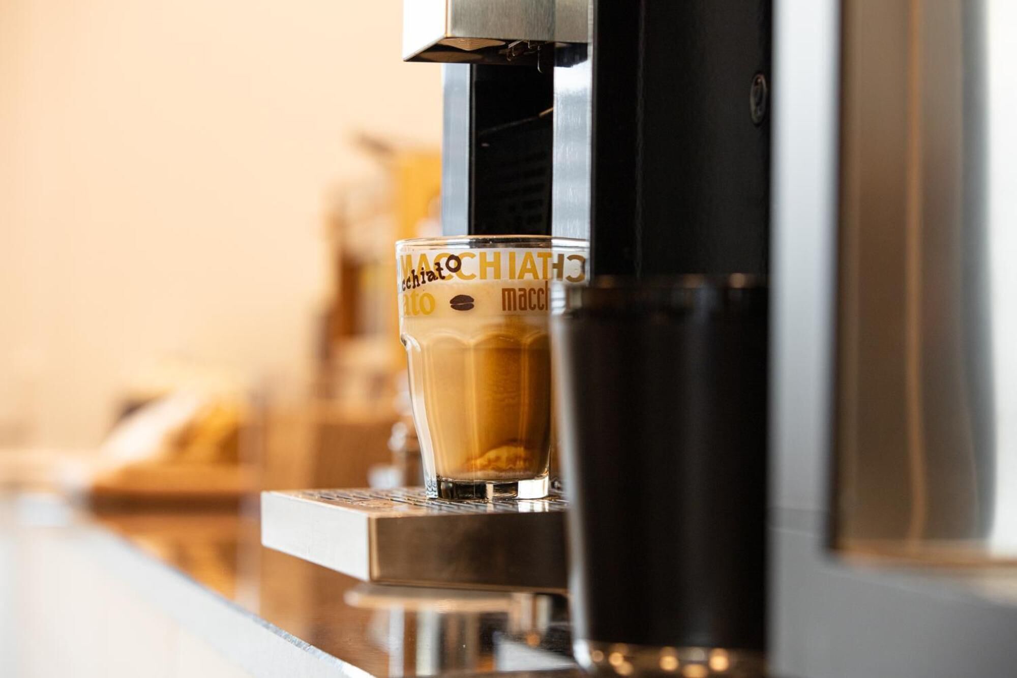 Gros plan sur une machine à café qui verse une dose de café dans un verre étiqueté « MACCHIATTO macchiato ».