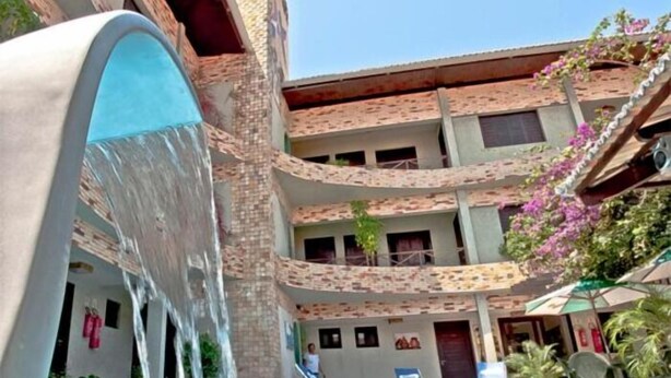 Piscina com cascata, edifício de vários níveis com varandas e área de estar ao ar livre.