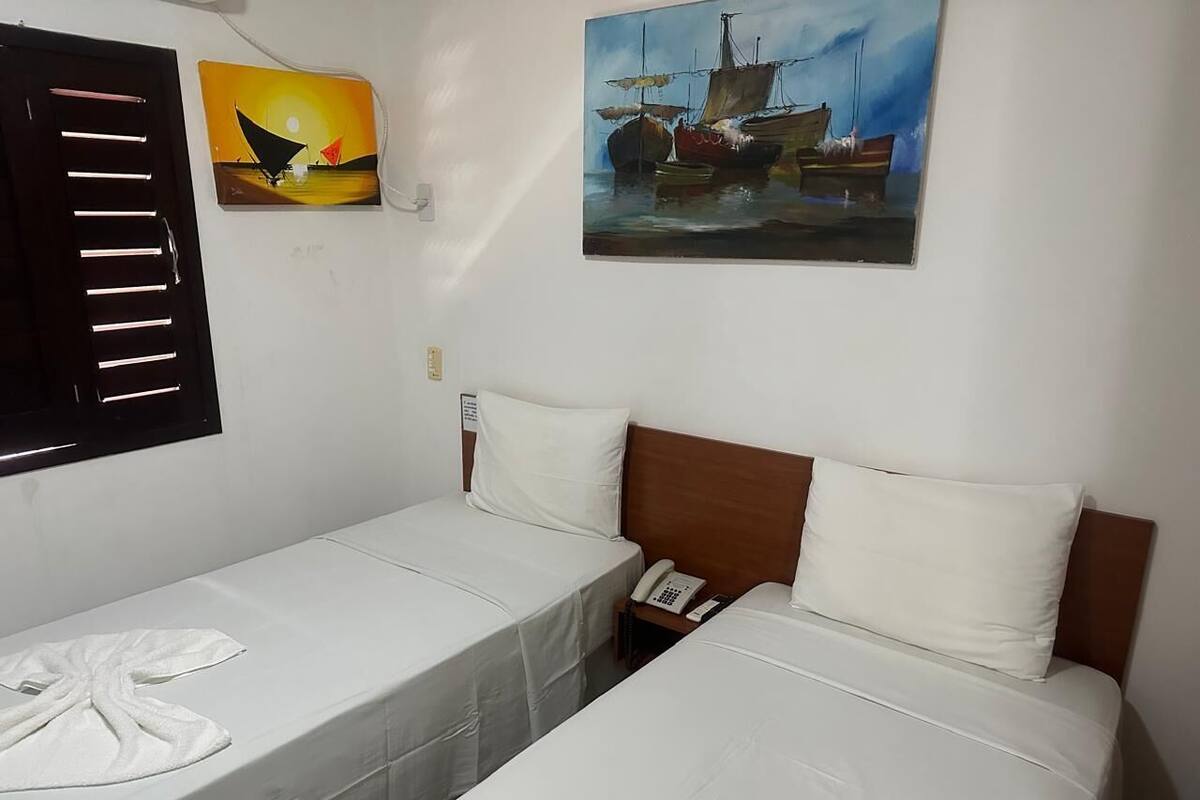A hotel room with two single beds, a wooden headboard, a white telephone, and a painting of boats on the wall.