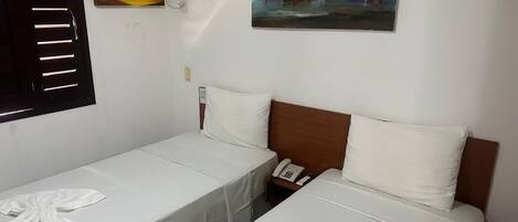Une chambre d’hôtel avec deux lits simples, une tête de lit en bois, un téléphone et un tableau représentant des bateaux accroché au mur.