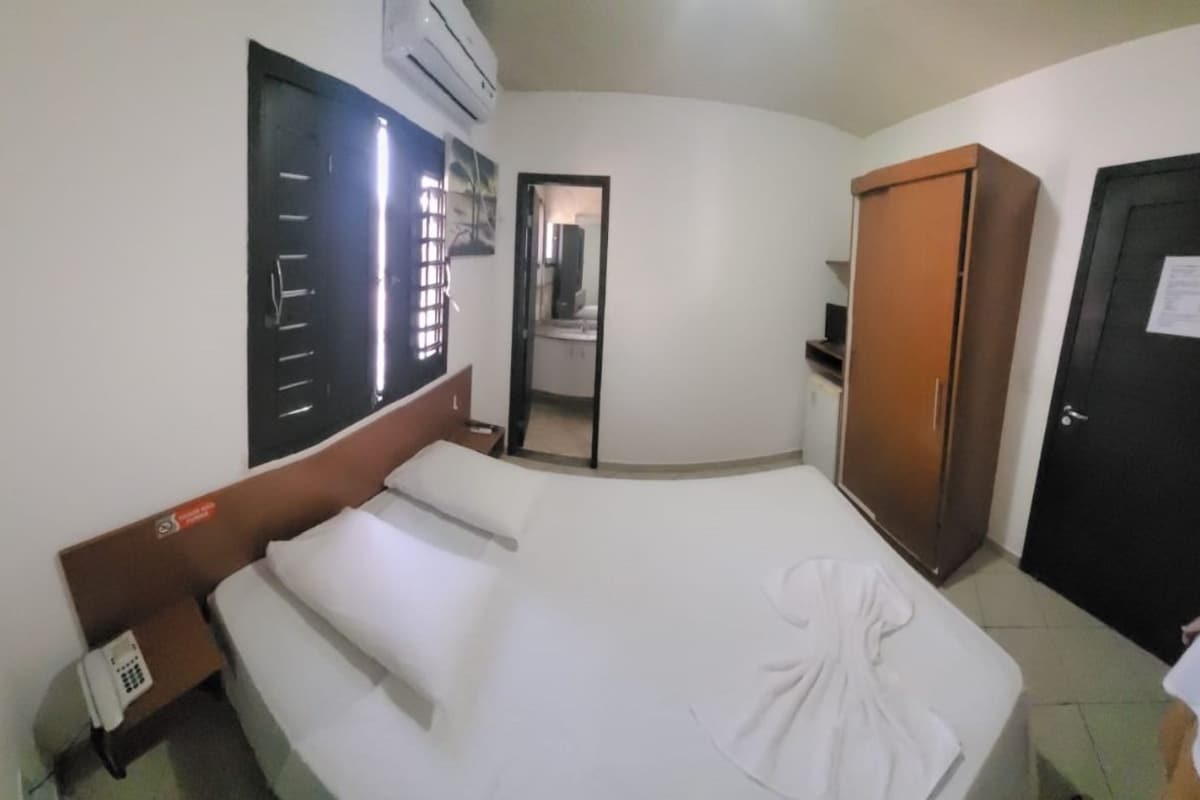 A hotel room with a bed, a wardrobe, a bathroom visible through an open door, and a small table with a phone.