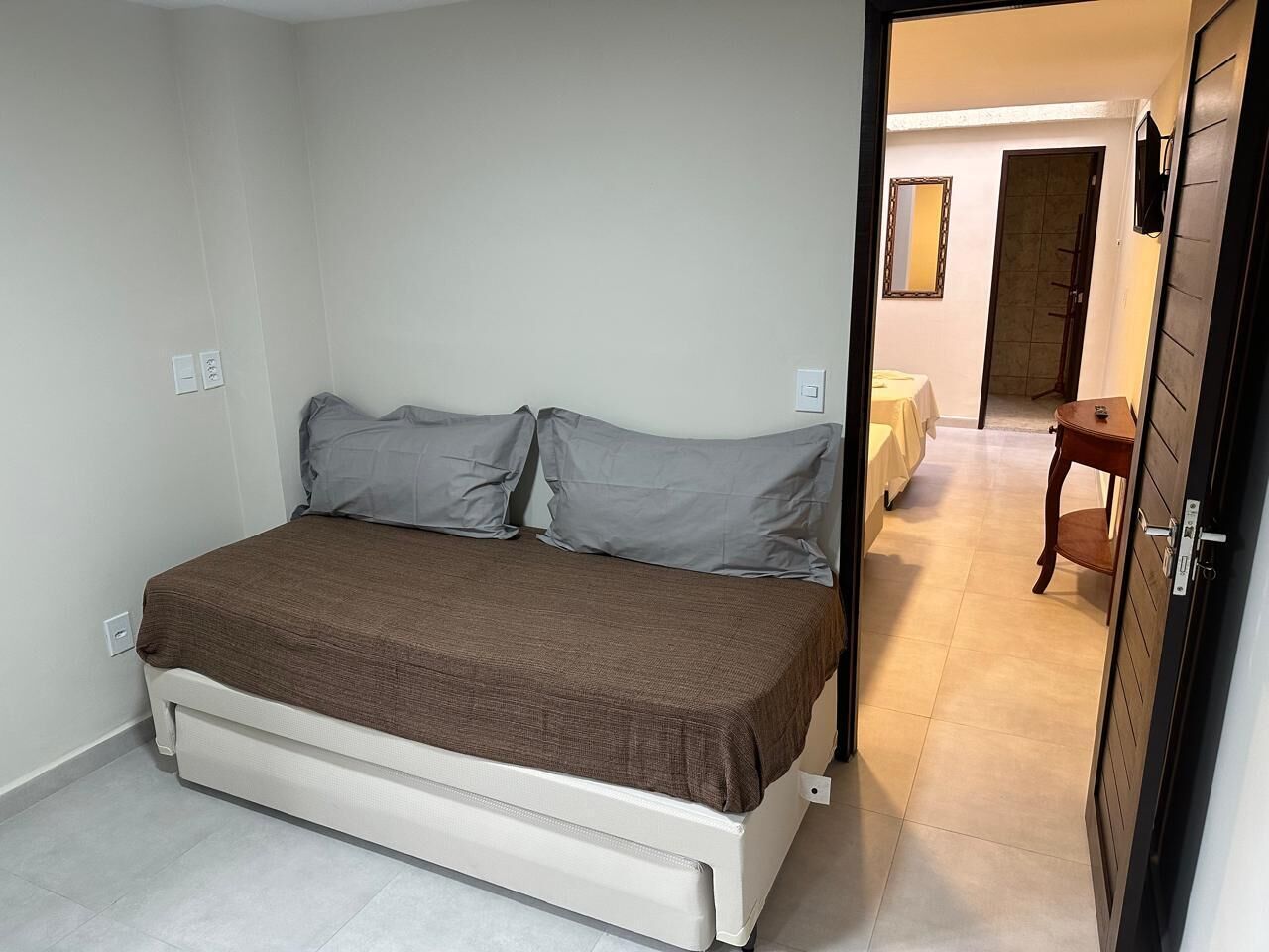 Un dormitorio con una cama, una mesita de noche y una puerta que da a otra habitación.