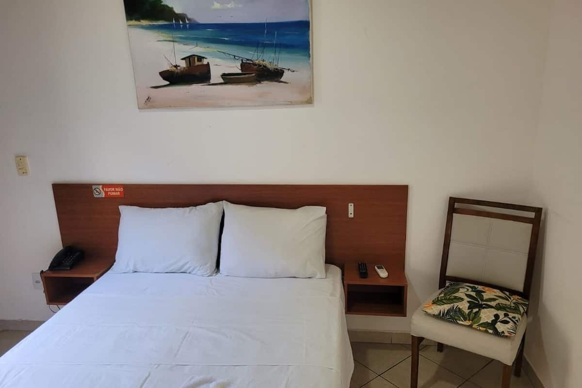 A hotel room with a bed, a nightstand, a chair, a painting of boats on a beach, and a sign indicating the room is for guests.