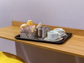 A breakfast tray with croissants, a coffee pot, and two white cups on a wooden table.