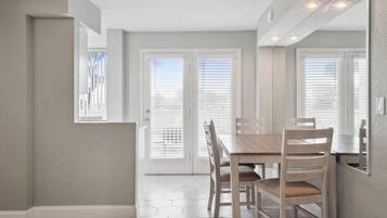 A dining area with a wooden table and chairs, a door with a view, and a light-colored wall.