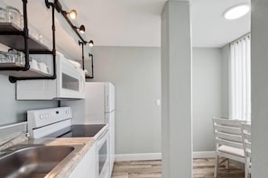 A modern kitchen with white appliances, a stainless steel sink, and a window providing natural light. - Howard Johnson by Wyndham Oceanfront Daytona Beach (Daytona Beach)