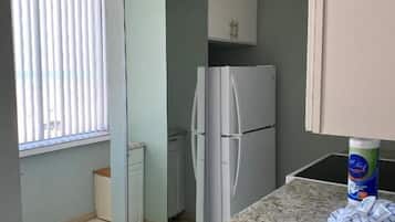 Una cocina compacta con un lavamanos de acero inoxidable, un refrigerador y una ventana con persianas.