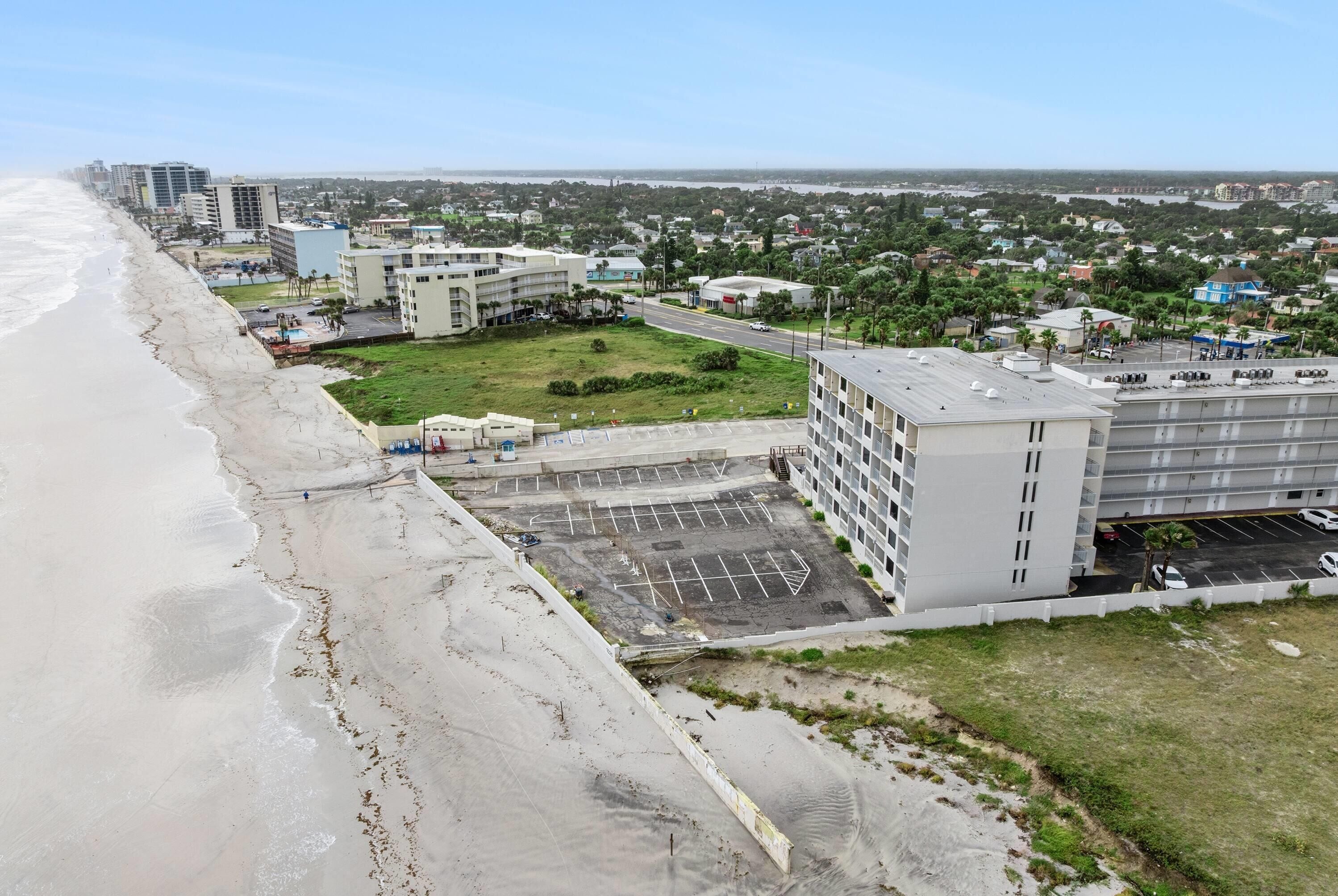A coastal hotel with a parking lot, a beach, and a view of the ocean.