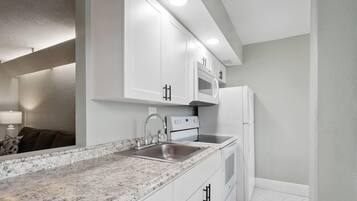 Una cocina moderna con gabinetes blancos, encimera de granito, electrodomésticos de acero inoxidable y microondas integrado.