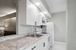 A modern kitchen with white cabinets, a granite countertop, stainless steel appliances, and a built-in microwave.