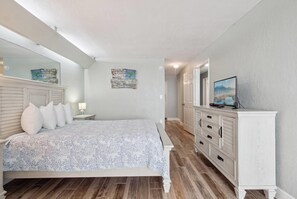 A bedroom with a bed, a dresser, a television, and a painting on the wall.
