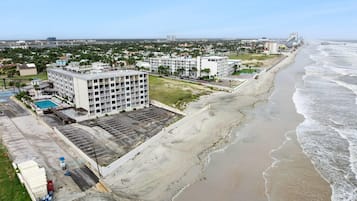A beachfront hotel with multiple buildings, a parking lot, and a beach.