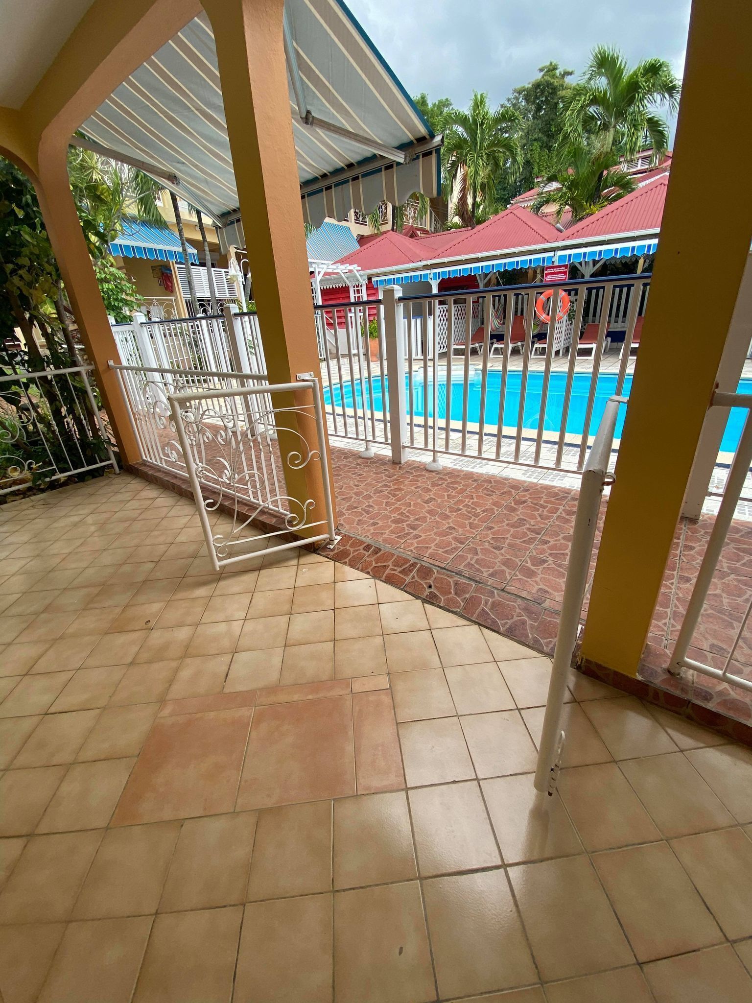 Un espace extérieur abrité doté d’une piscine, de rampes en métal blanc et d’un sol carrelé.