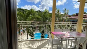Ein überdachter Balkon mit Fliesenboden, weißen Stühlen, einem Tisch und einem blauen Sessel.