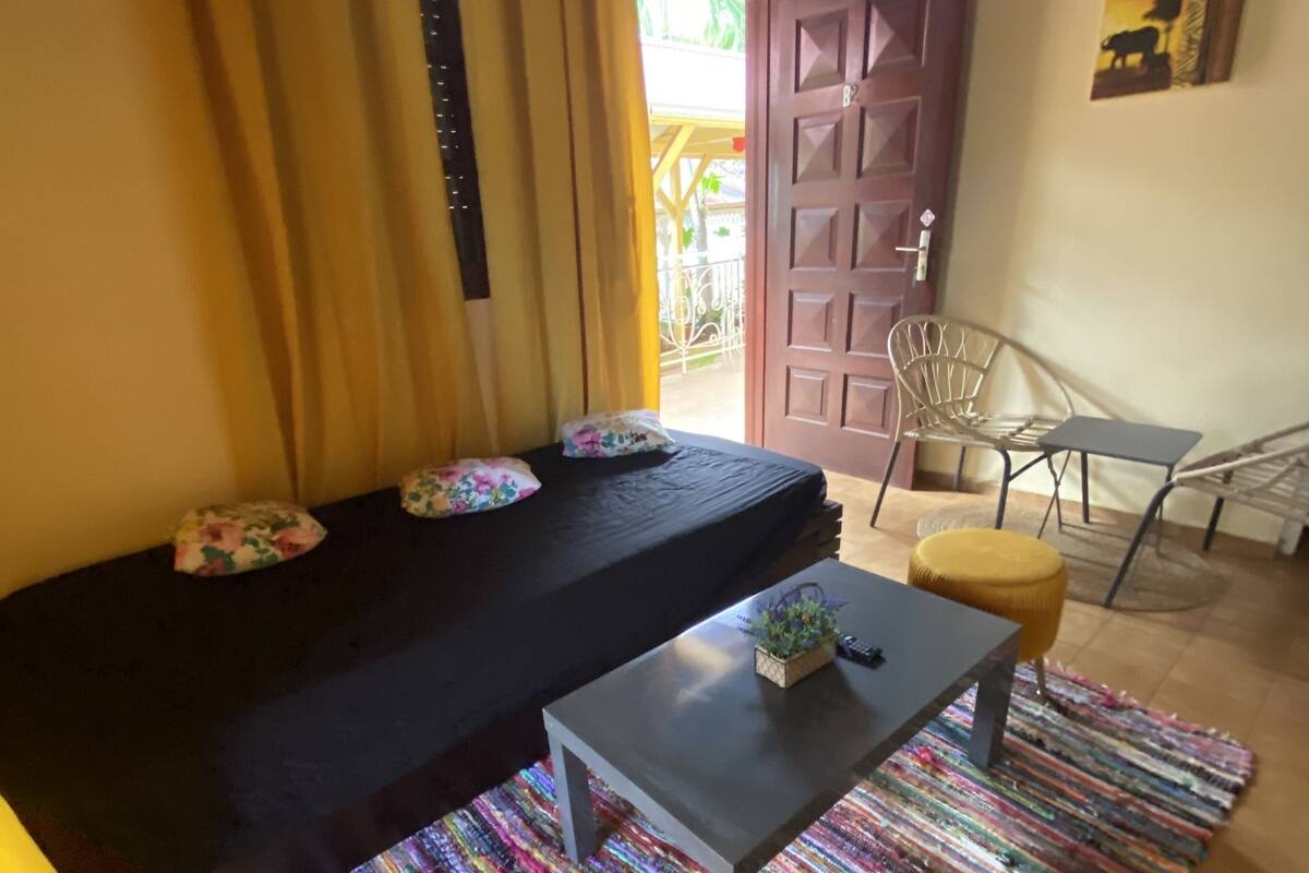 Una habitación con un sofá negro, una mesita, una alfombra colorida y una silla.
