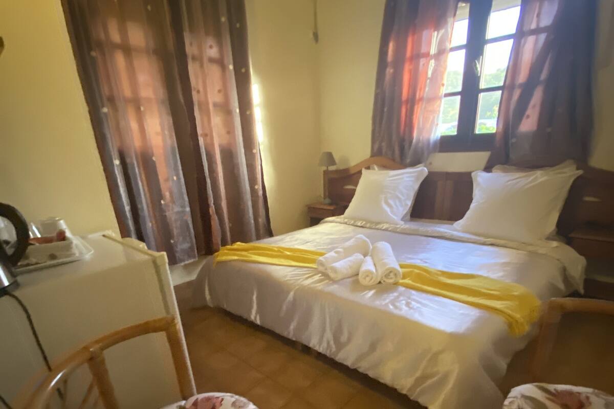 Un dormitorio con cama, dos sillas, una mesita de noche y una ventana con cortinas.