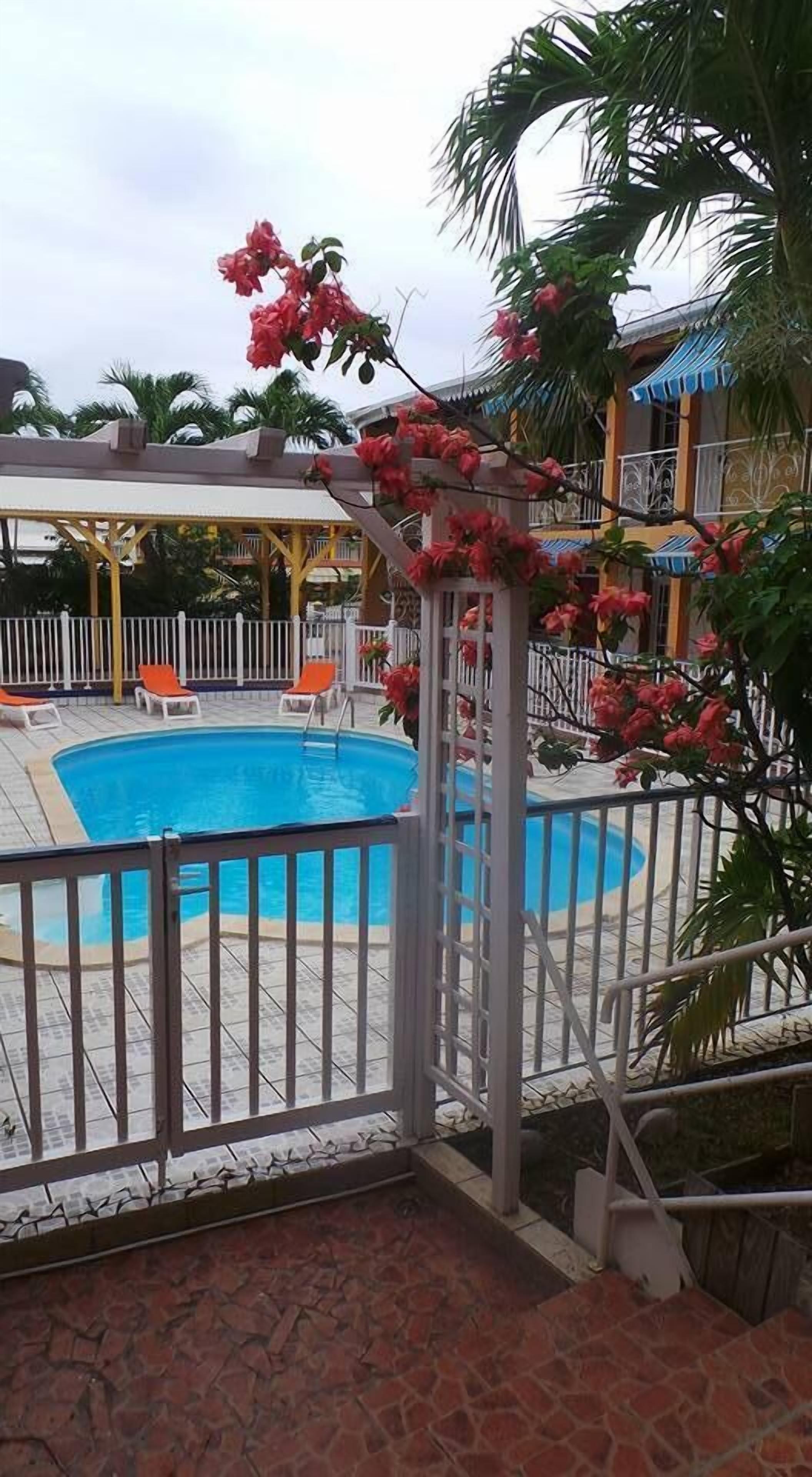 A swimming pool with a white fence, surrounded by lounge chairs and a covered area with a blue awning.