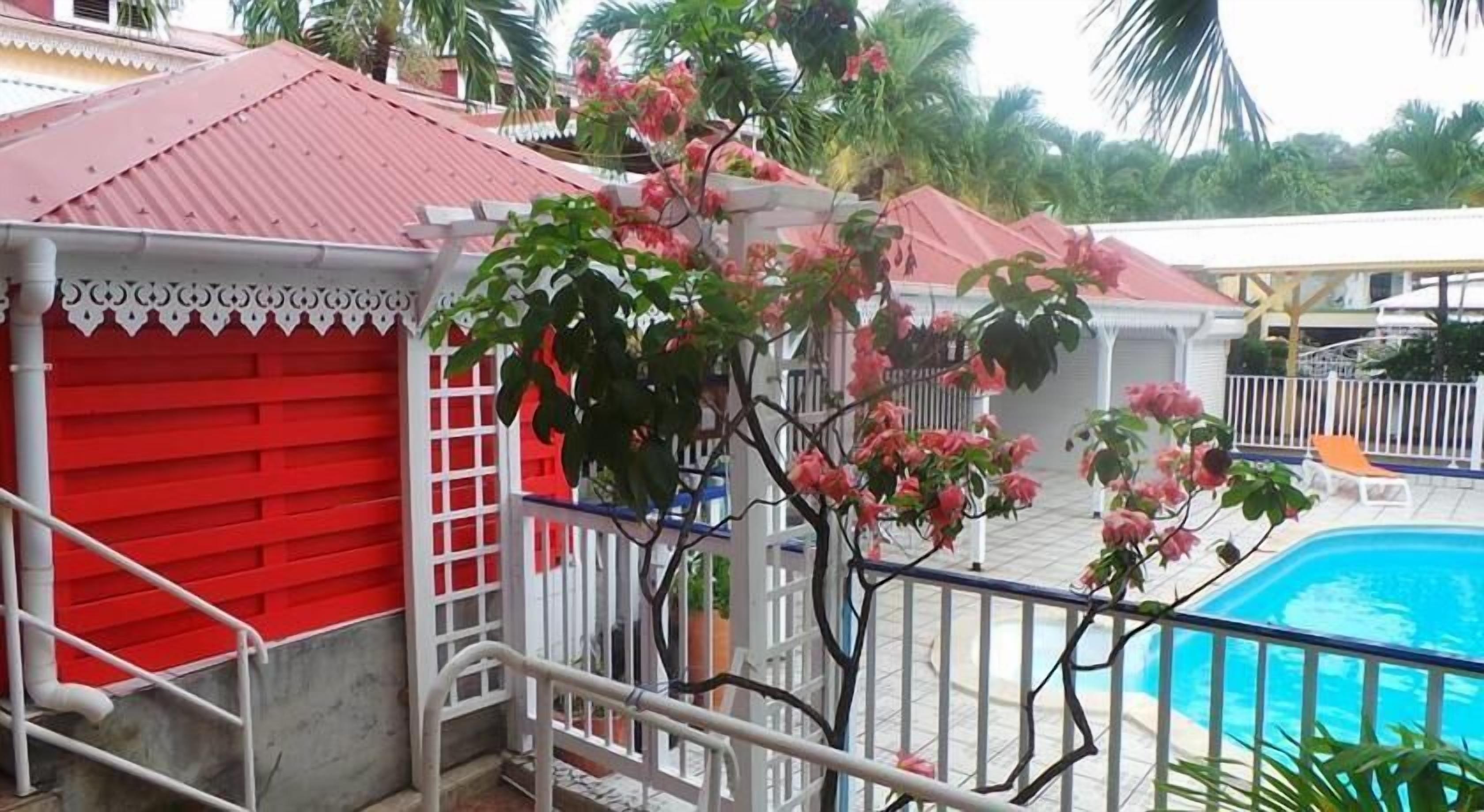 Un área de piscina con un edificio rojo, barandillas blancas y flores rosadas.