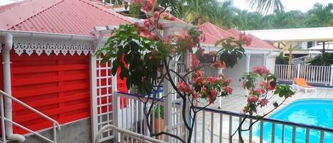 Un área de piscina con un edificio rojo, barandillas blancas y flores rosadas.