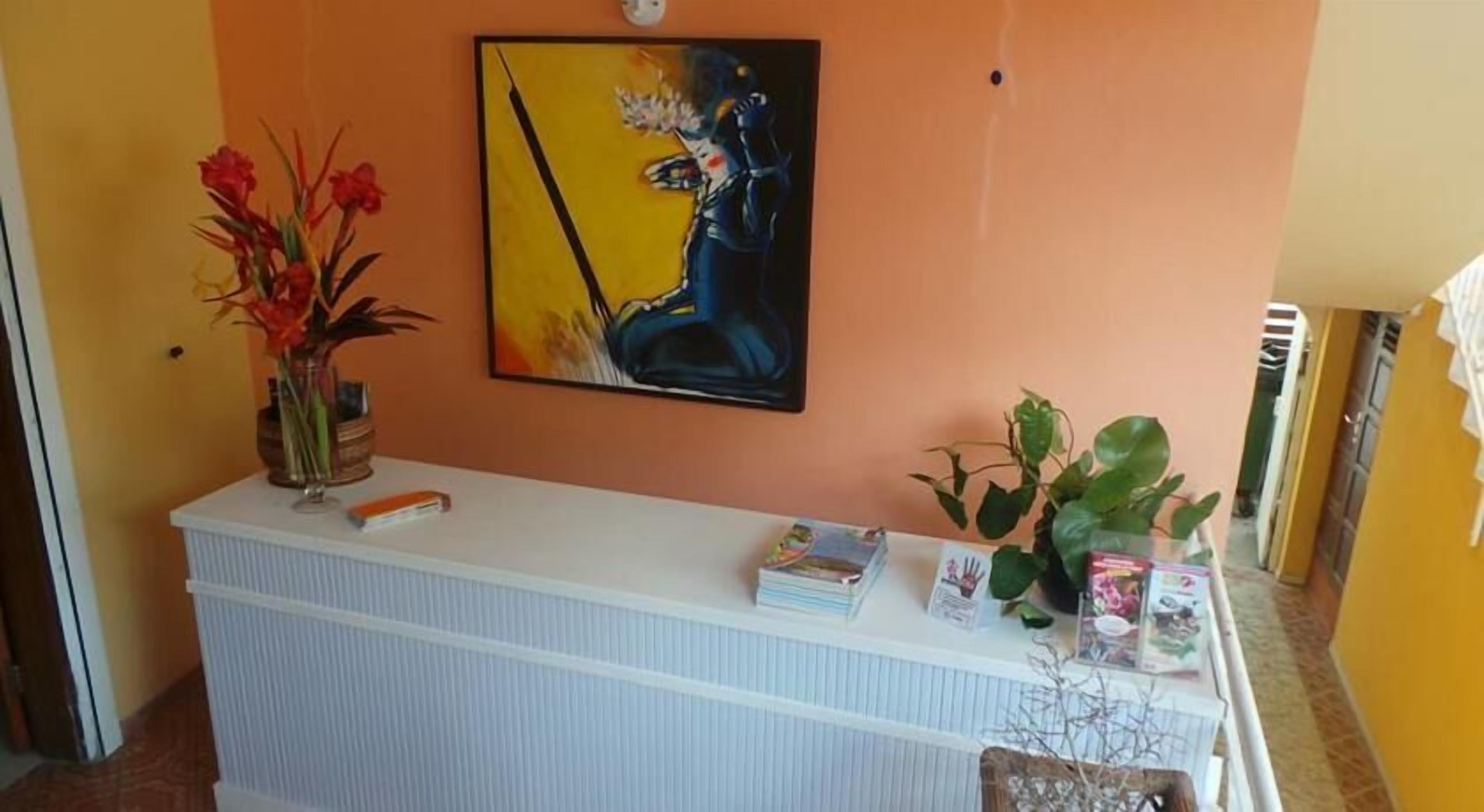 A reception desk with a vase of red flowers, a painting, and a plant.