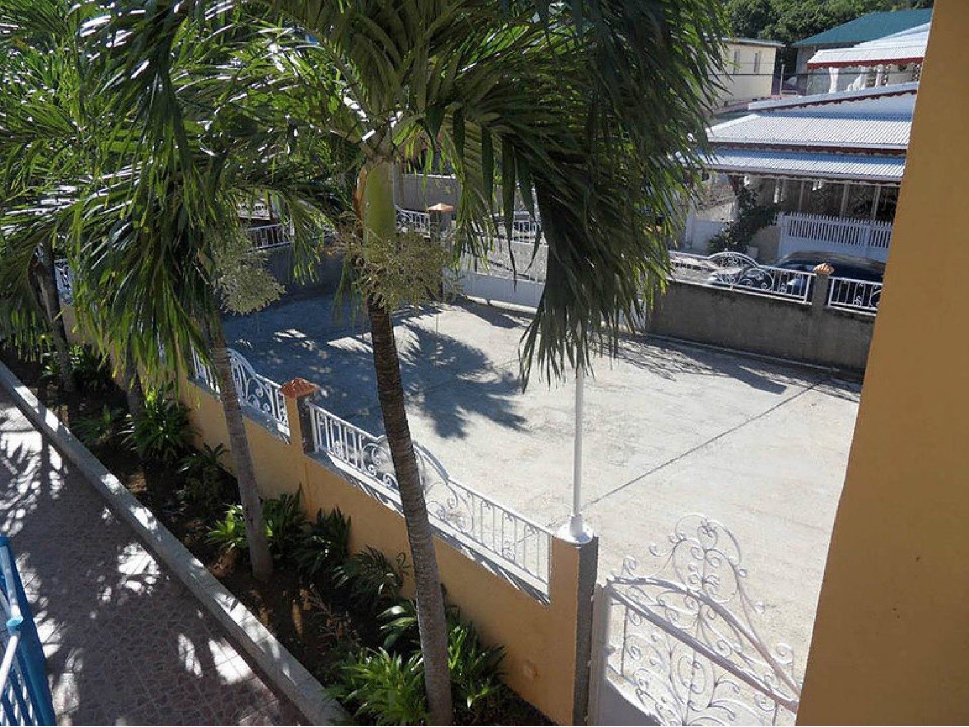 Un patio con suelo empedrado, palmeras y un edificio con cerramiento de metal.