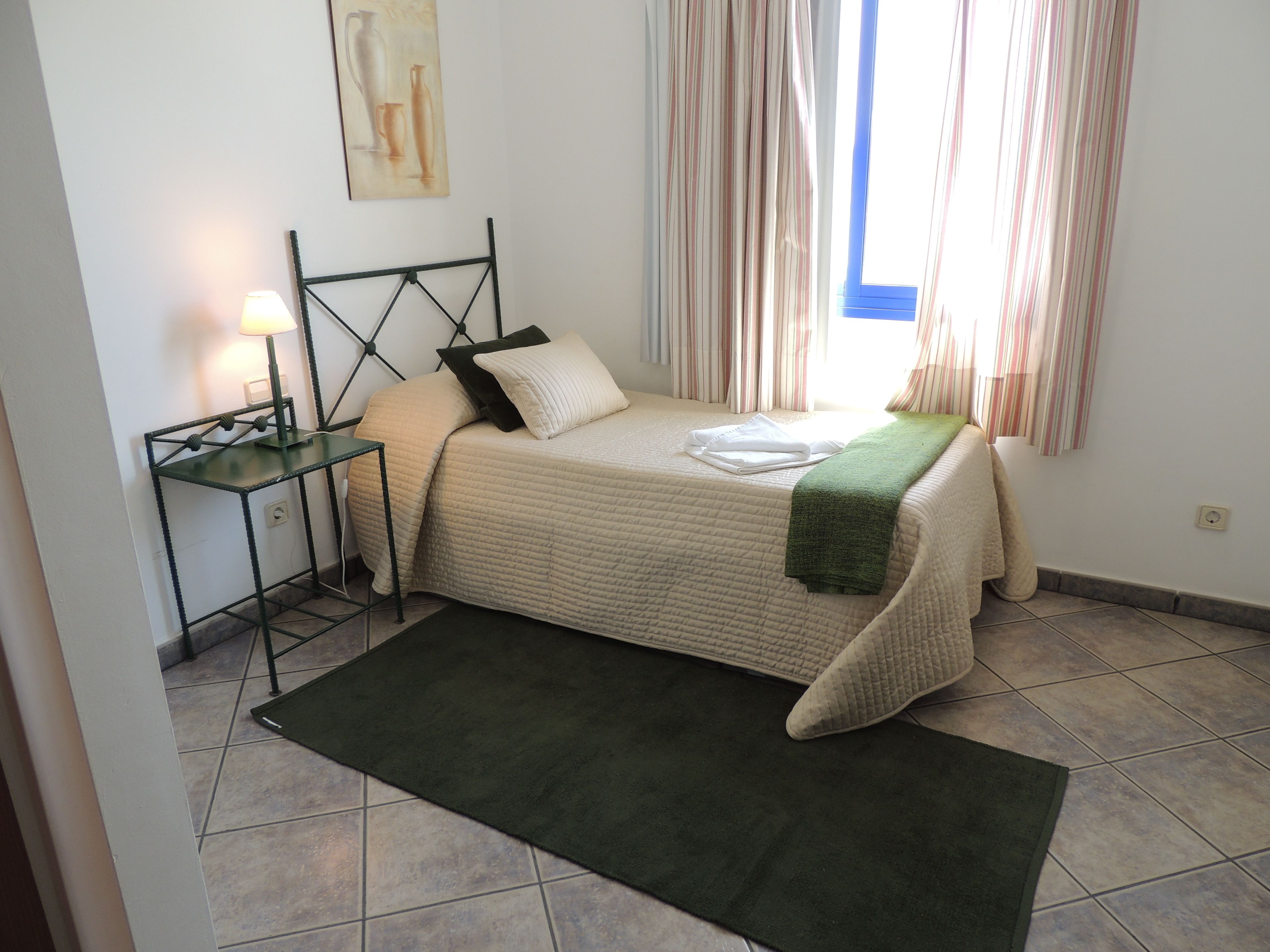 A neatly arranged bedroom with a bed, bedside table, lamp, and a window with curtains.