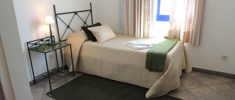 A neatly arranged bedroom with a bed, bedside table, lamp, and a window with curtains.