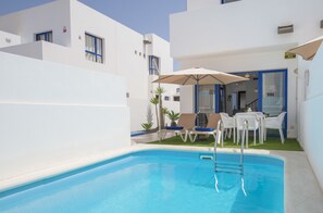 A pool area with a ladder, white lounge chairs, and a table with umbrellas. - Villas Puerto Rubicon (Yaiza)