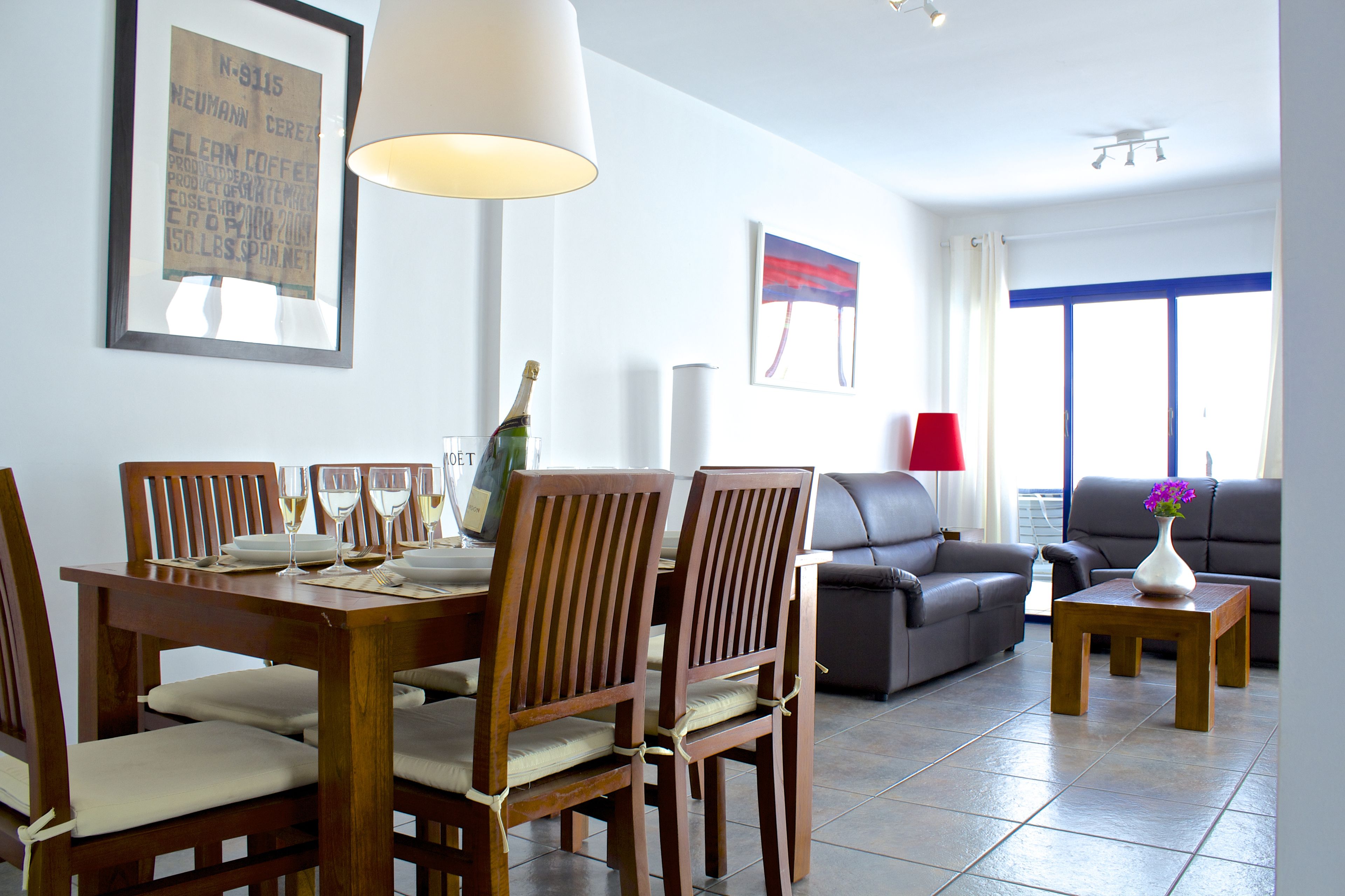 A dining area with wooden chairs and a table set for a meal, a sofa, and a small table with a vase.