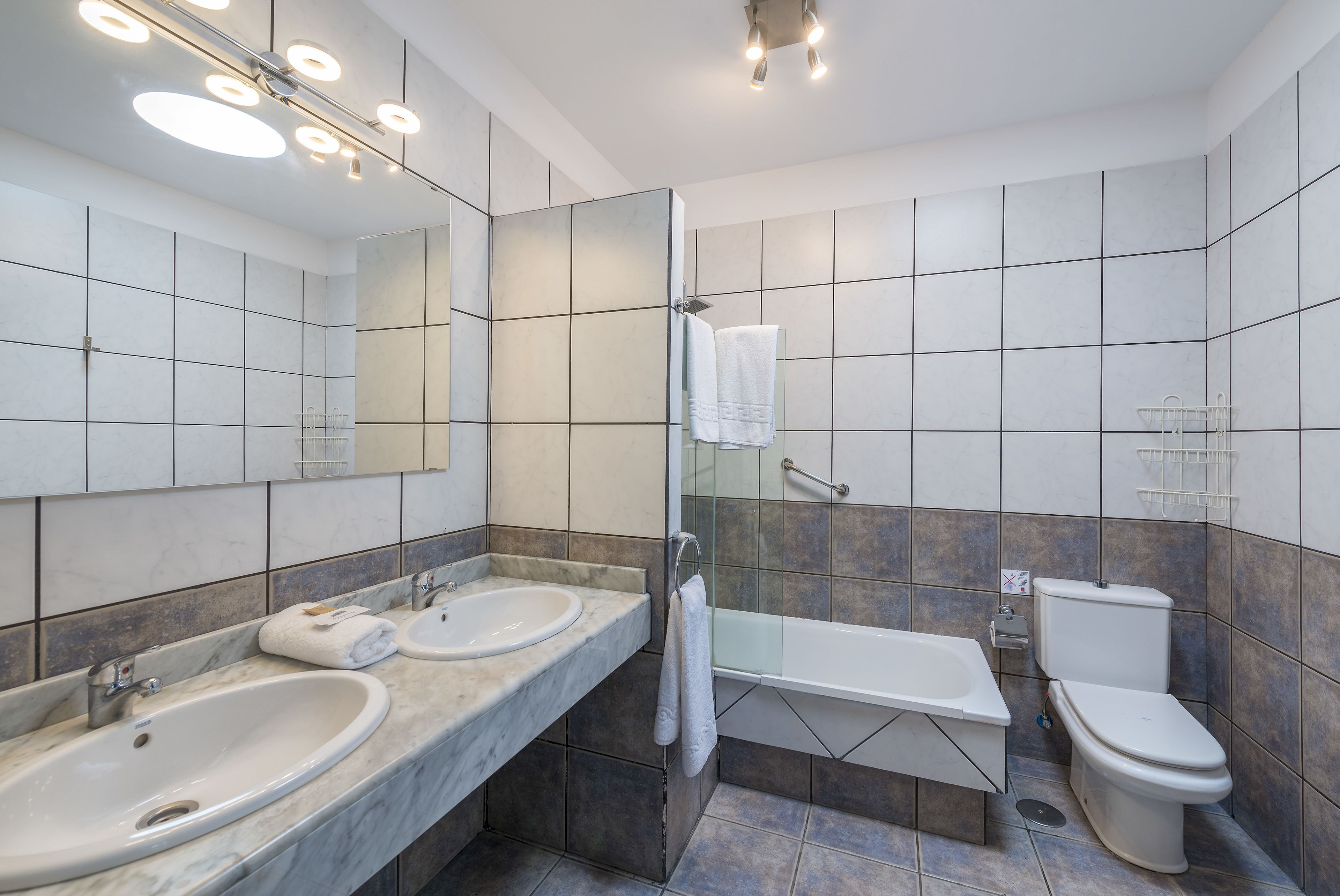 A modern bathroom with two sinks, a bathtub, and a toilet.