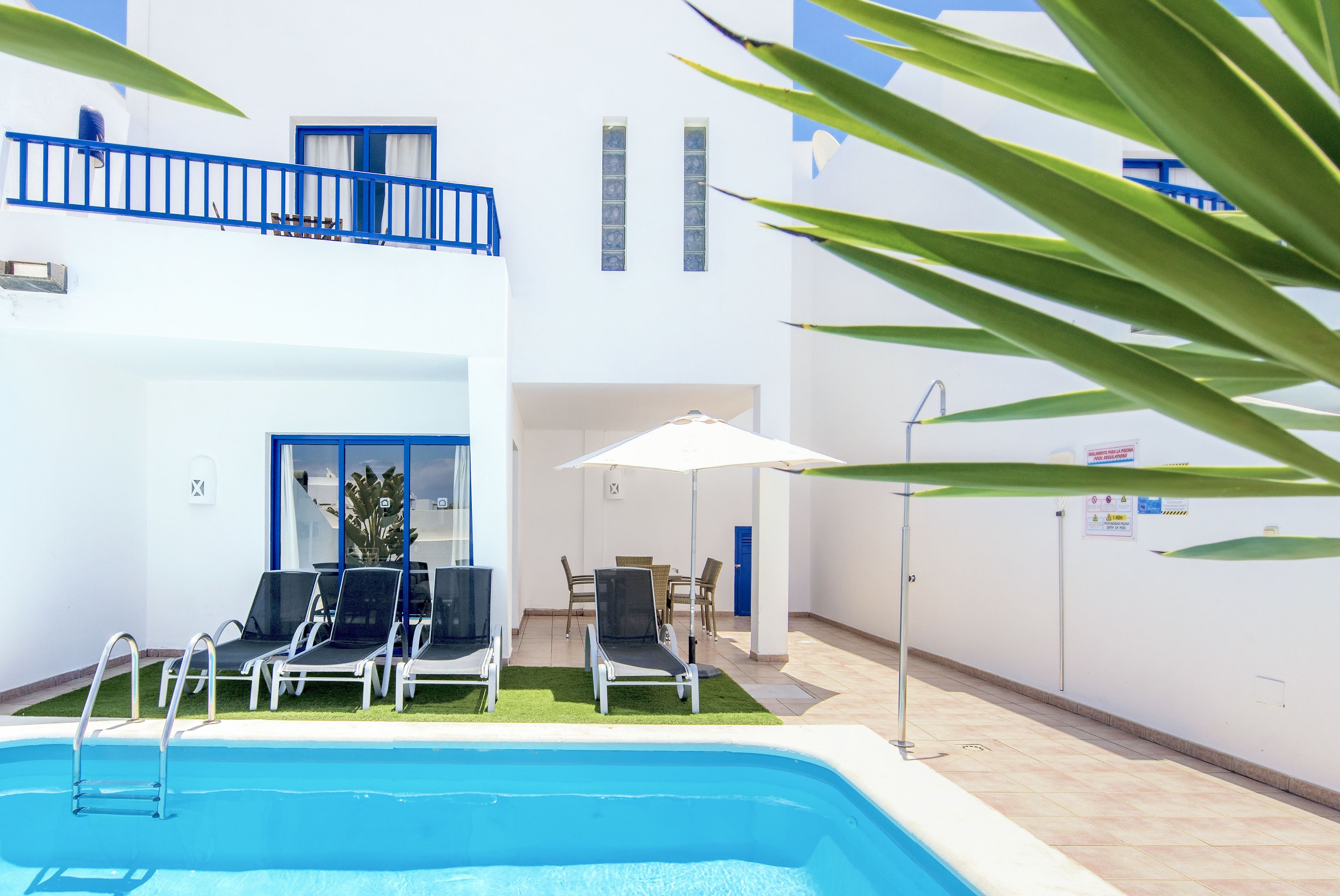 Área de piscina com espreguiçadeiras, mesa e guarda-sol.