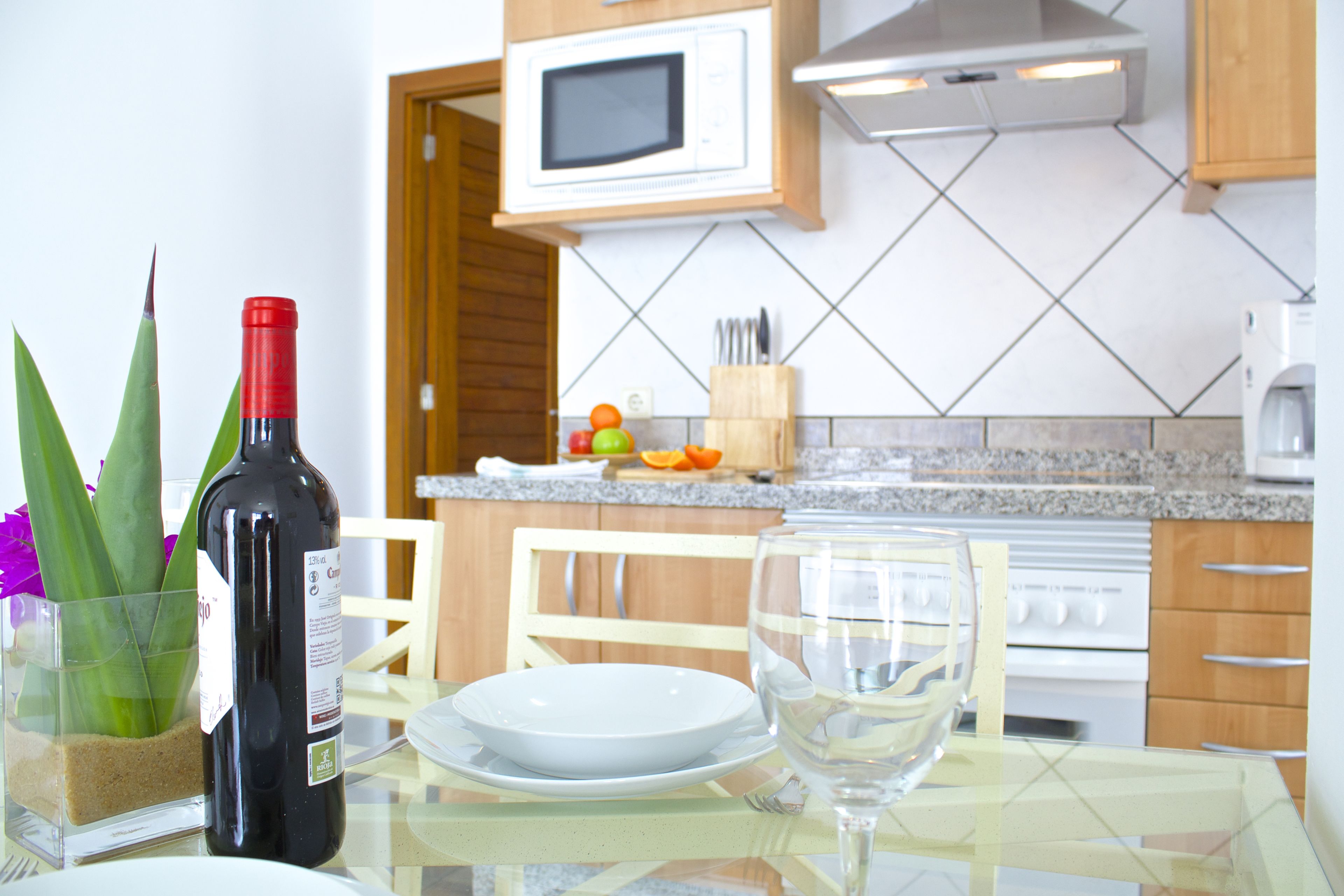 A dining table with a wine bottle, a glass, and a plate. There is a microwave above the counter and a stove in the background.