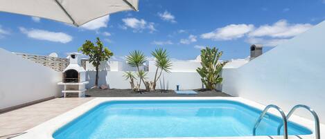 Una piscina con sillones de descanso y zona de barbacoa.